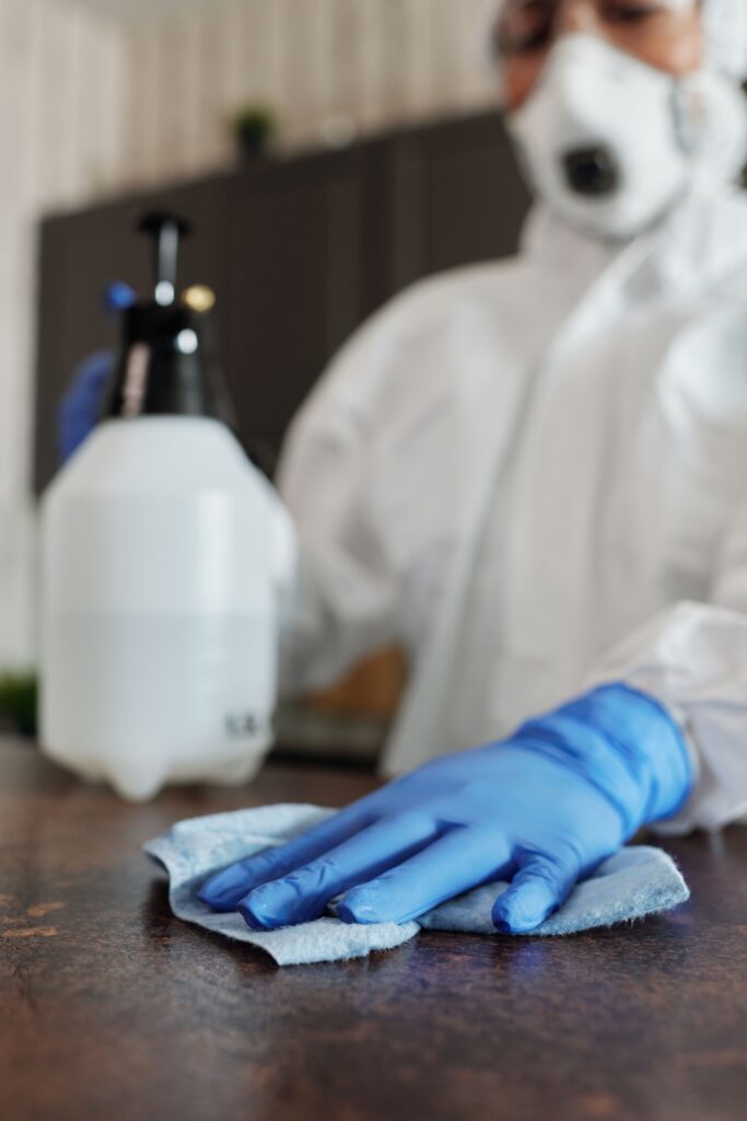 Technicien en tenue de protection désinfectant une table avec une lingette