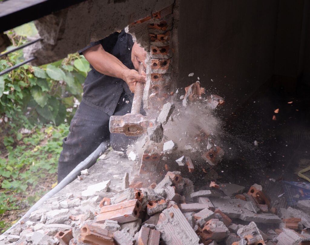 Ouvrier abattant un mur de briques à la masse